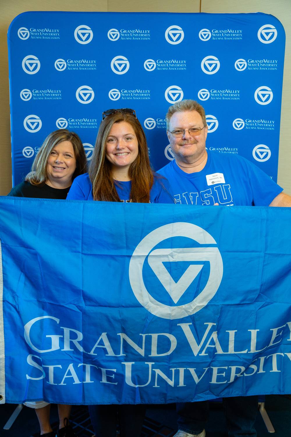 Two alumni and one student pose for a photo with the GV flag